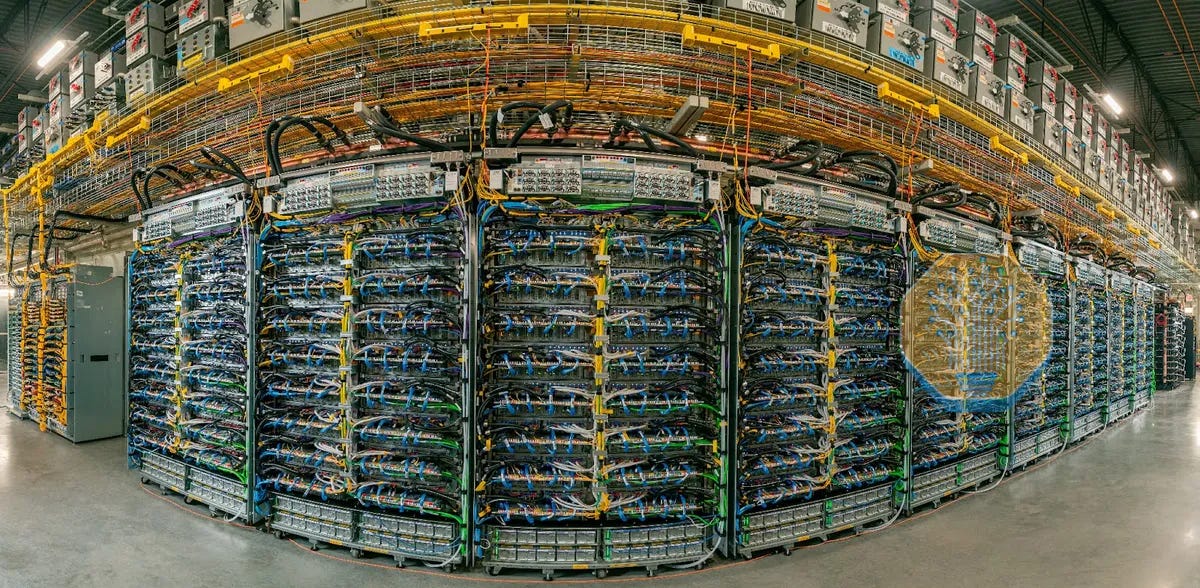 A fisheye view of a data center wall with rows of server racks, complex cabling and overhead cable trays.